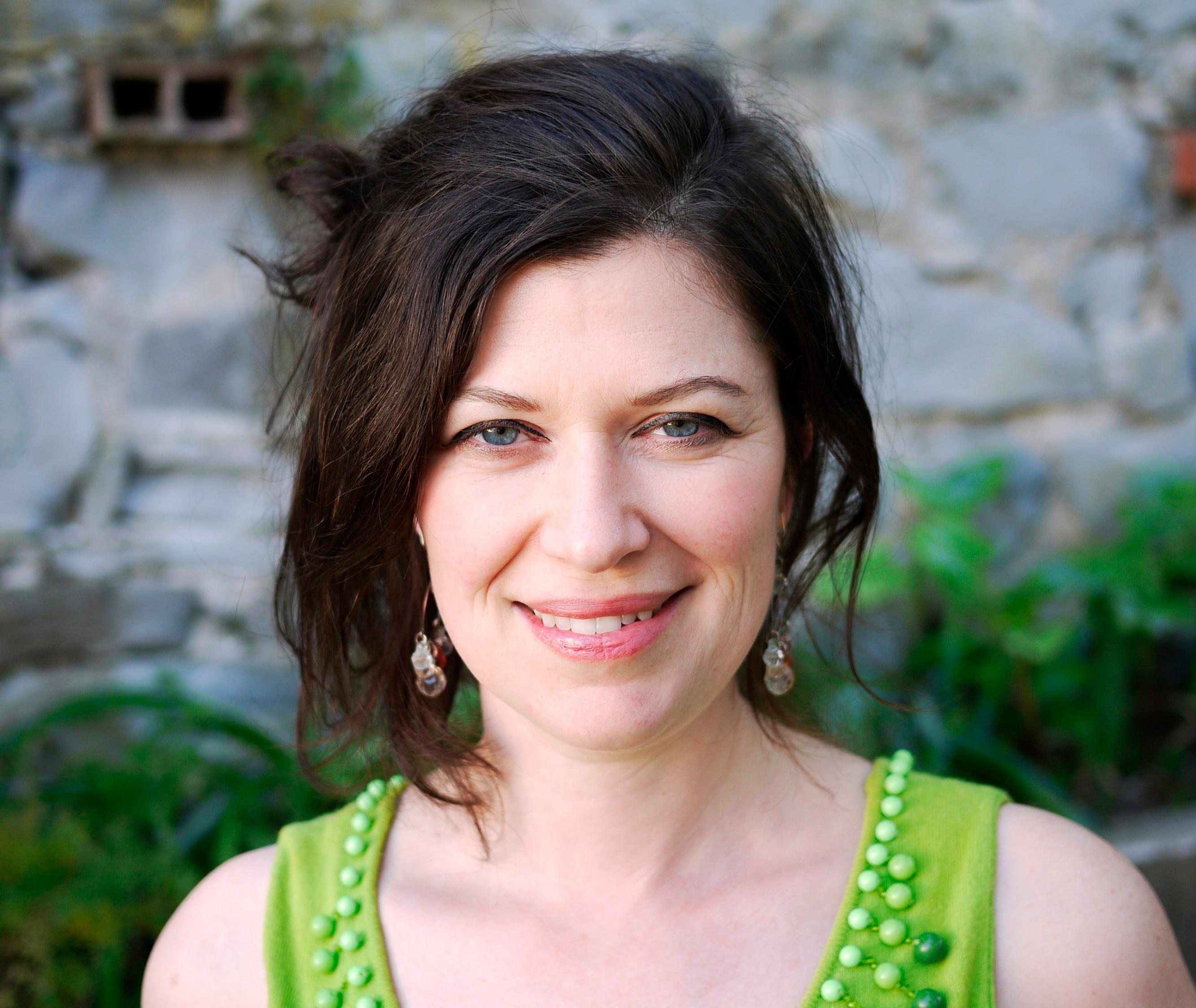 Anna Fitch smiles directly at the camera. She has dark hair and is wearing a green top.