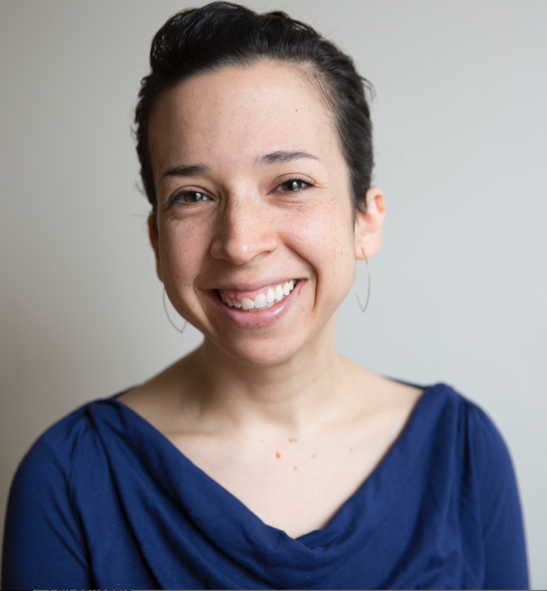Danielle, a white woman in a blue top and hoop earrings, smiles