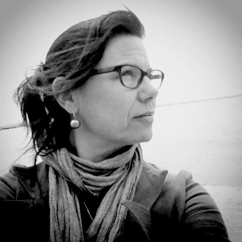 Elisa Paloschi faces away from the camera. Her hair is in a ponytail and she wears eyeglasses. The photo is in Black and White.