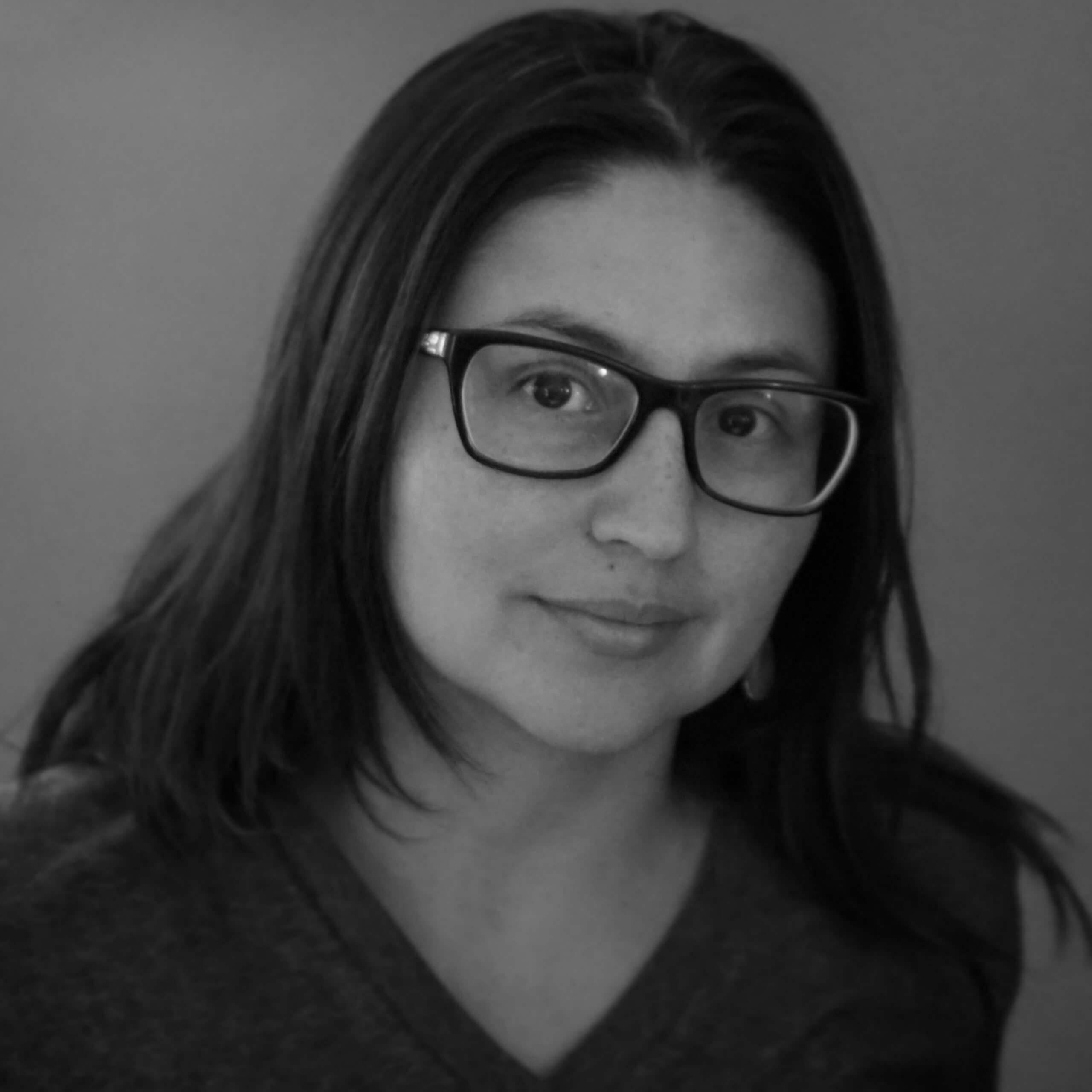 Cristina Ibarra looks directly at the camera and smiles. She wears black eyeglasses.