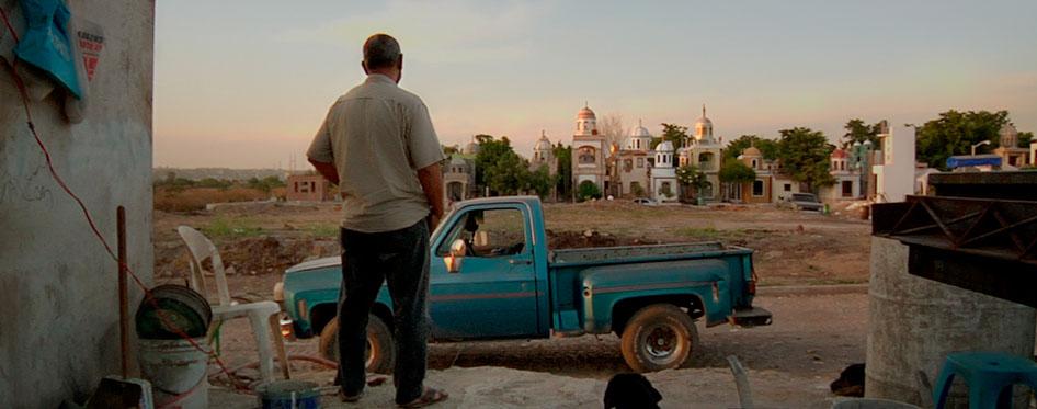 man looks at blue truck amongst a landscape of a town.
