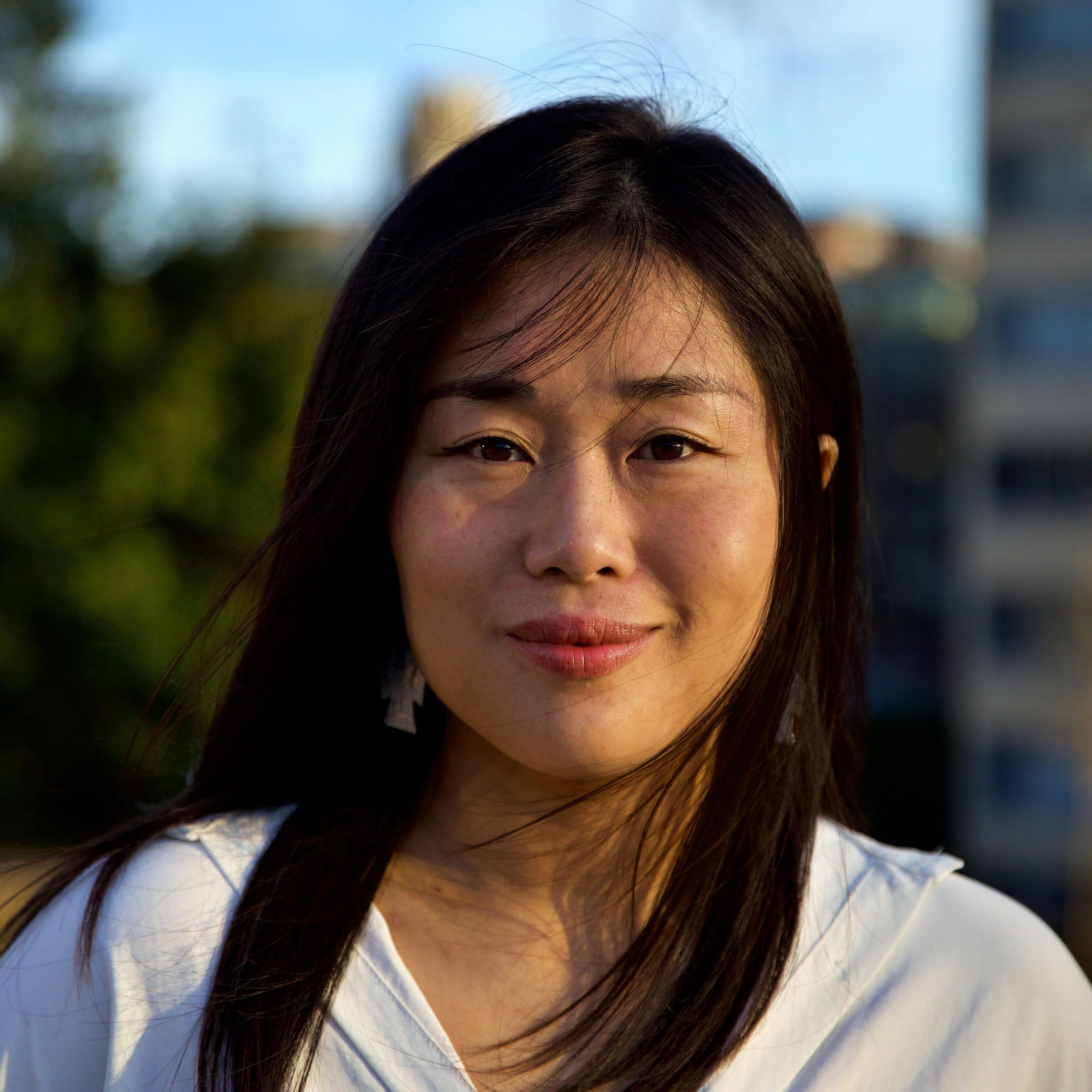 Director/Producer Xinyan Yu, an Asian woman with black hair and black eyes in a white silky shirt.