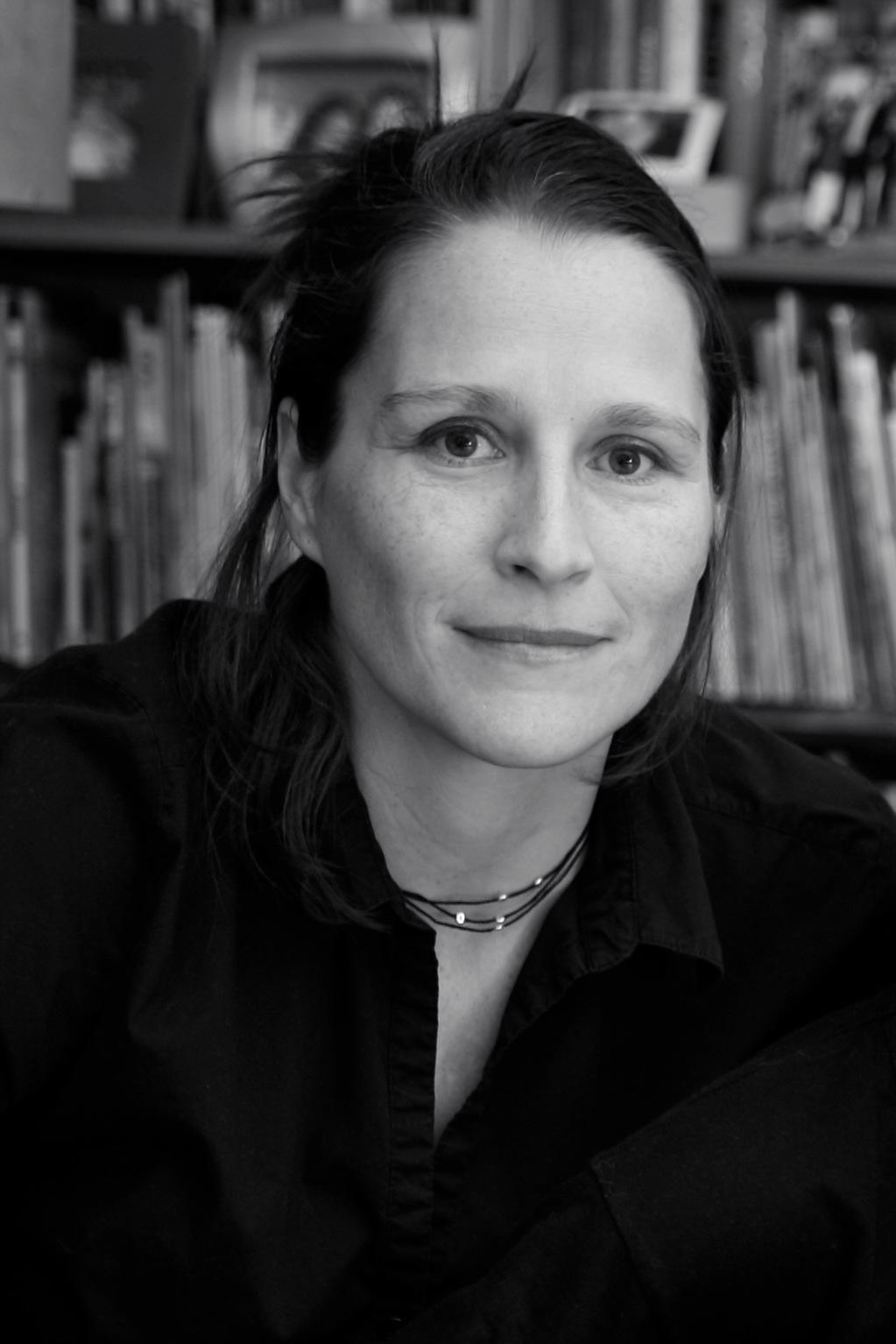 Black and White photo of Catherine Gund. Catherine smiles at the camera with her hair pulled back and she is wearing a black shirt.