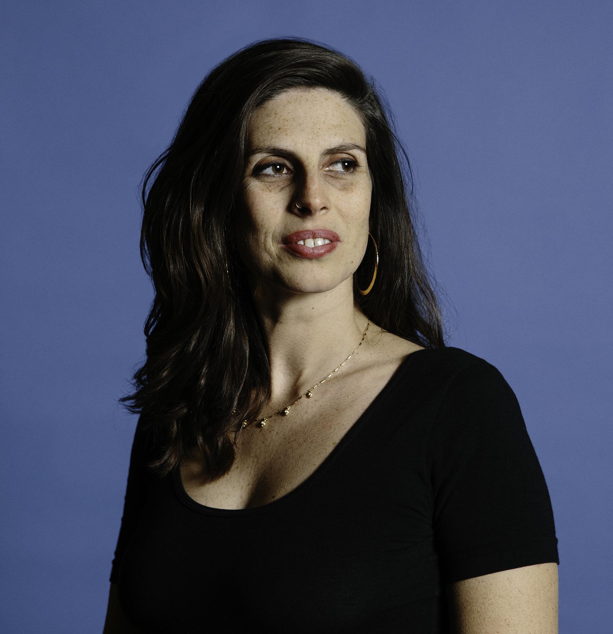 Portrait of Zara Katz, a woman with medium hair, wearing a black shirt with a necklace and looking to the left away from the camera.
