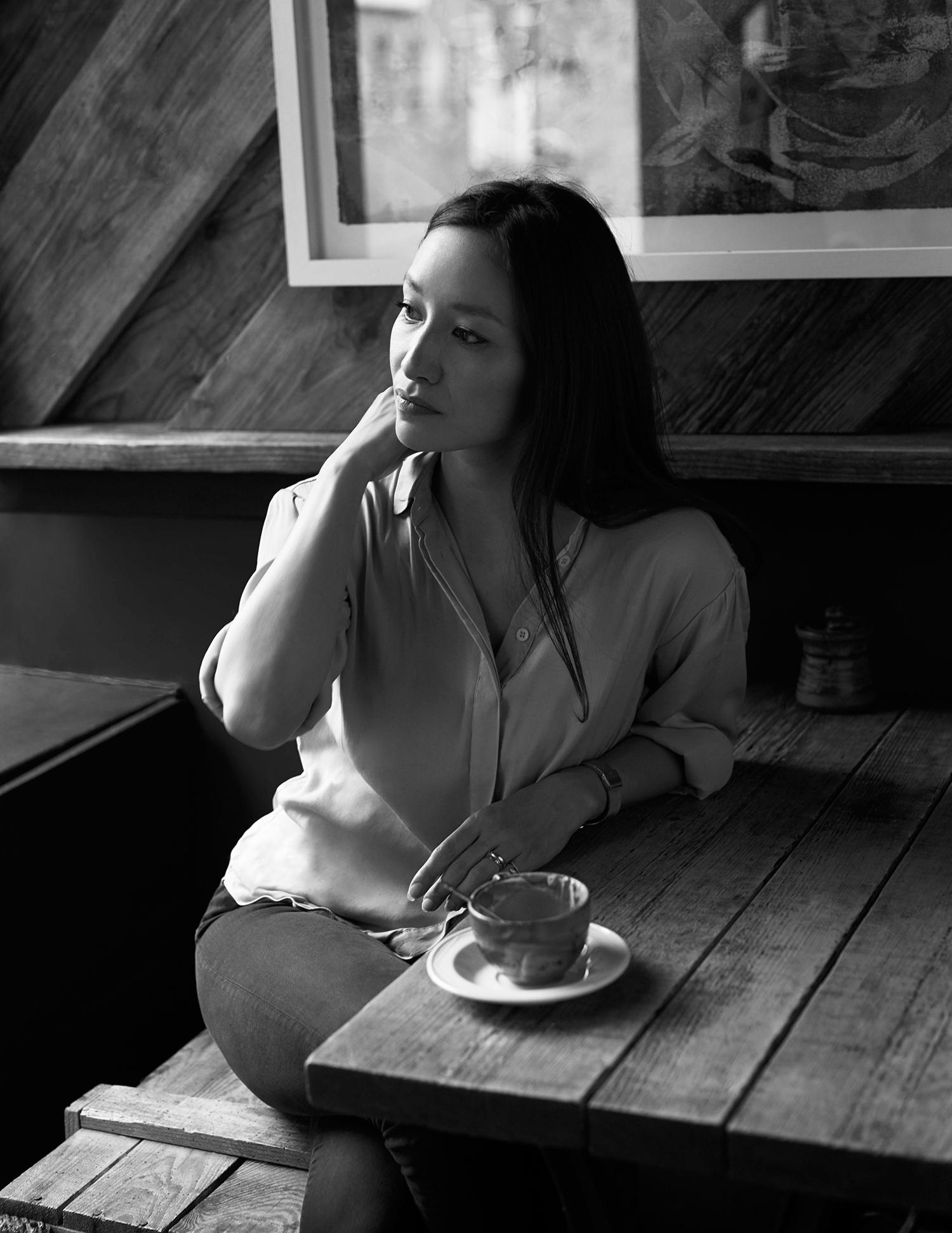 A black and white portrait of a woman sitting in a cafe with a cup of coffee.