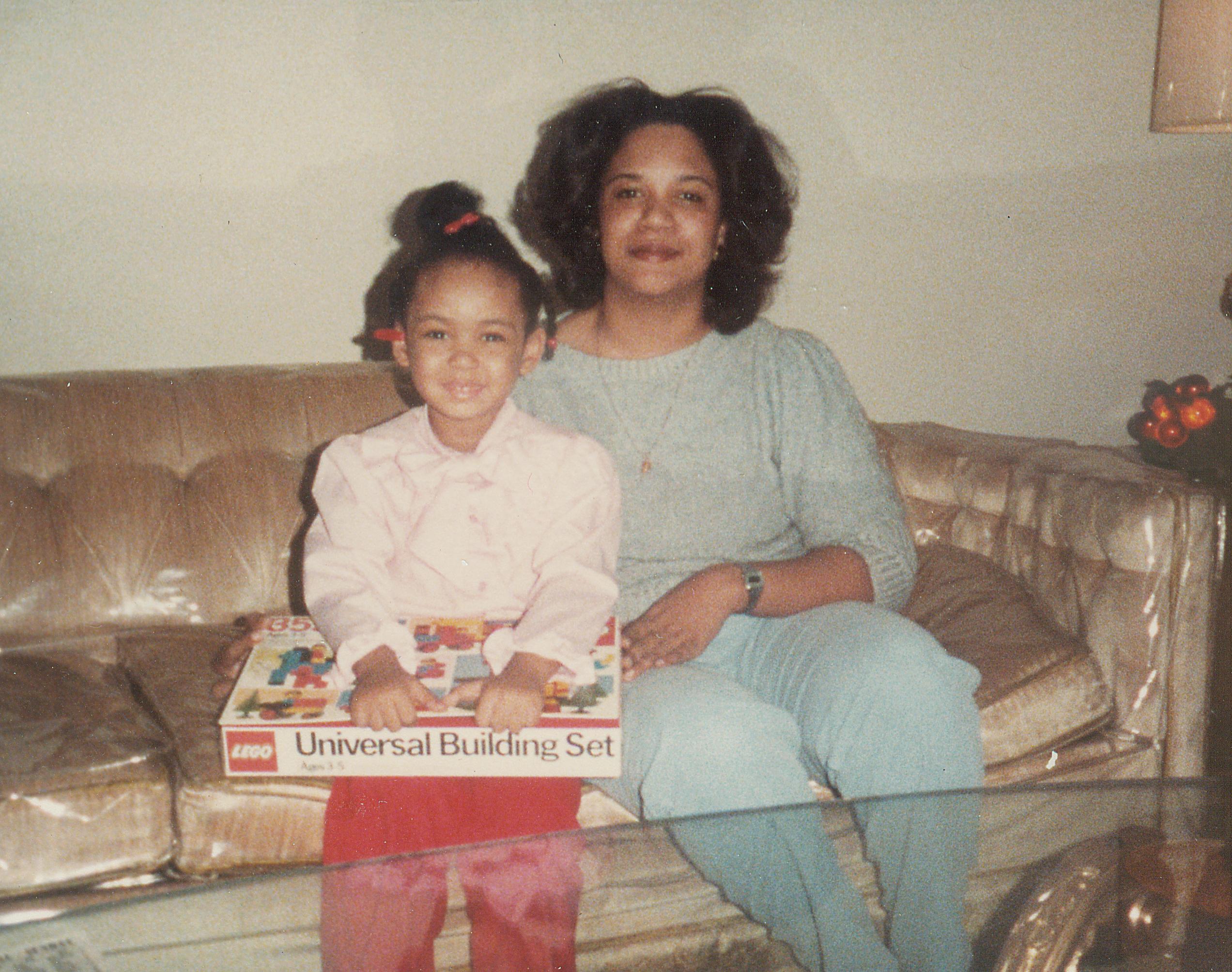 An archival photo of a young girl and her mom sitting on a couch with a lego set.