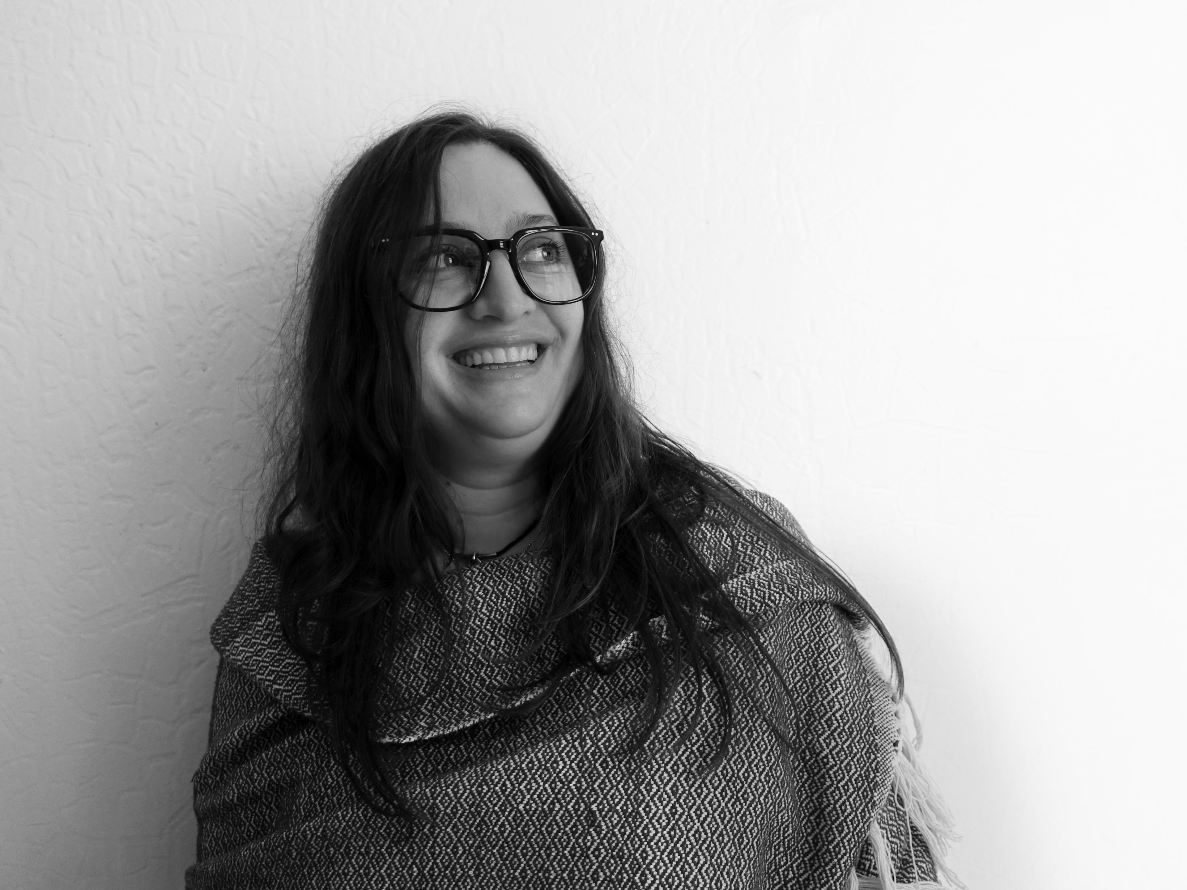 Portrait of a woman with medium long hair, thick black frames and laughing and looking away from the camera
