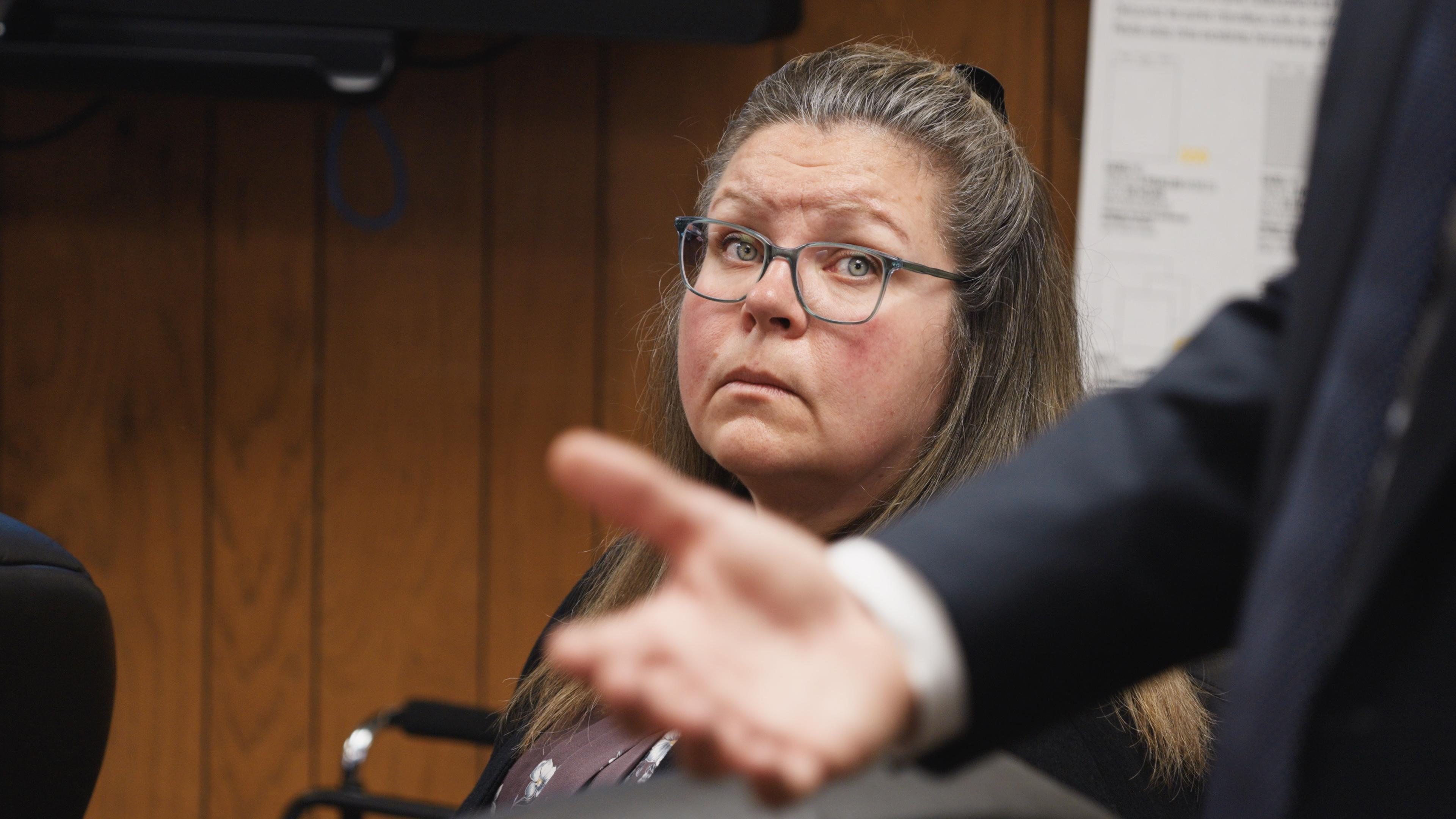 A woman sits in a court room and looks over at an attorney.