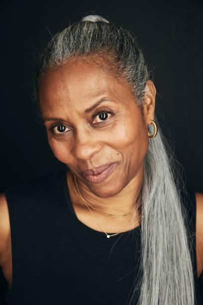 Brown-skinned Black woman with silver hair in a long ponytail.