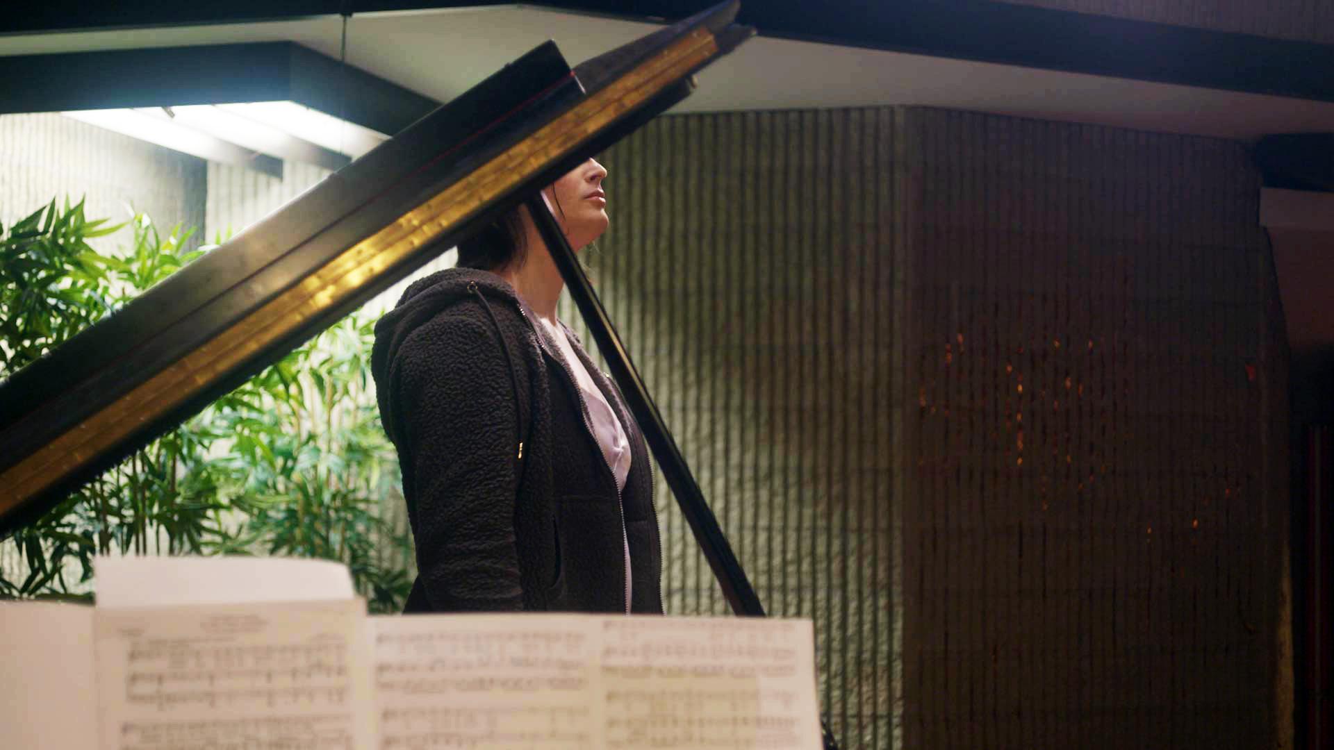 A piano partially obscures the face of a woman on a stage in an opera hall.