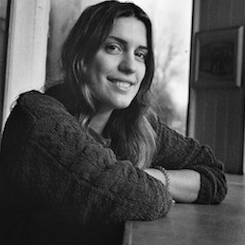 Nadja crosses her arms on top of a table. She looks at the camera and smiles.