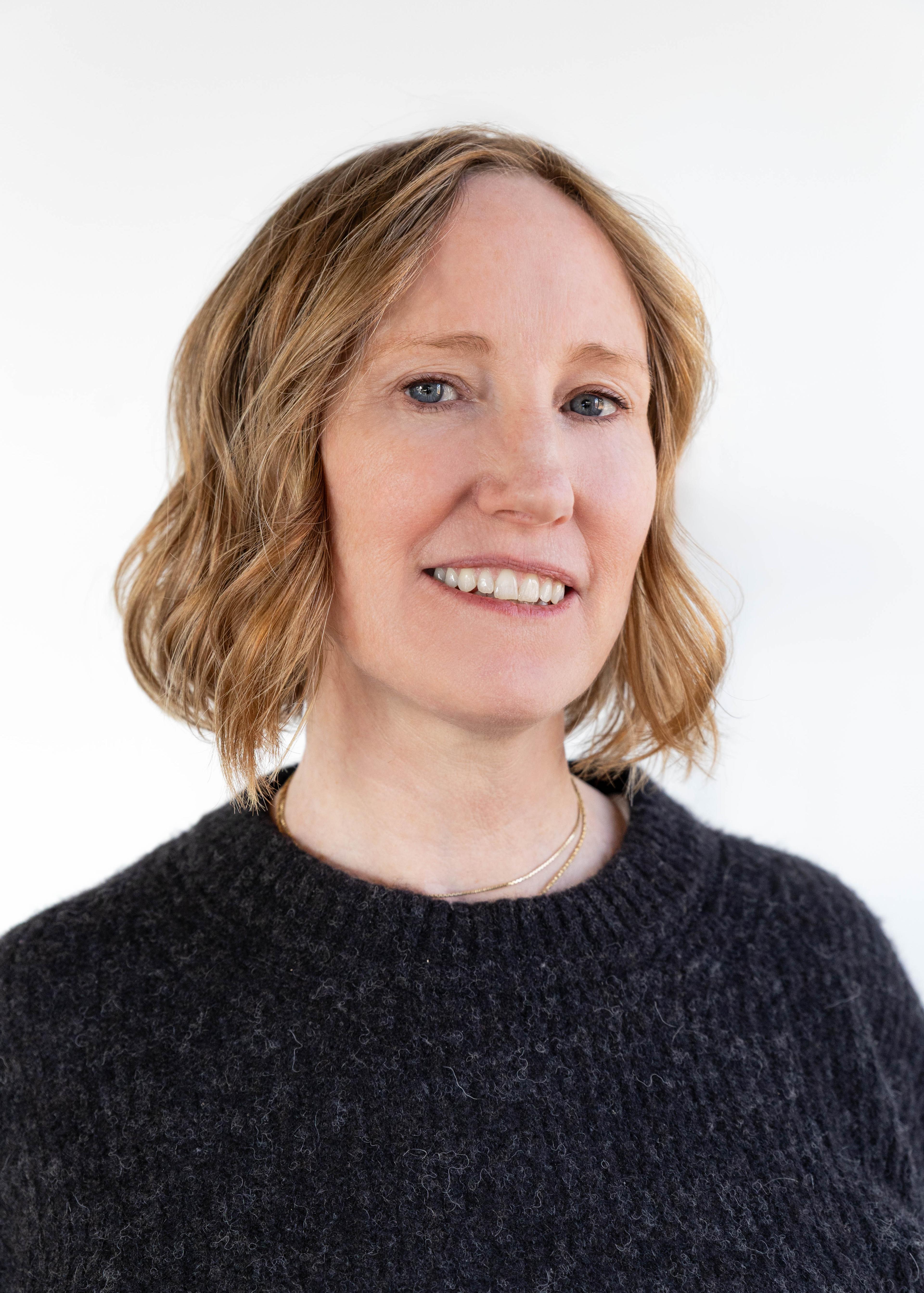 A woman with short, wavy hair wearing a dark sweater smiles at the camera.