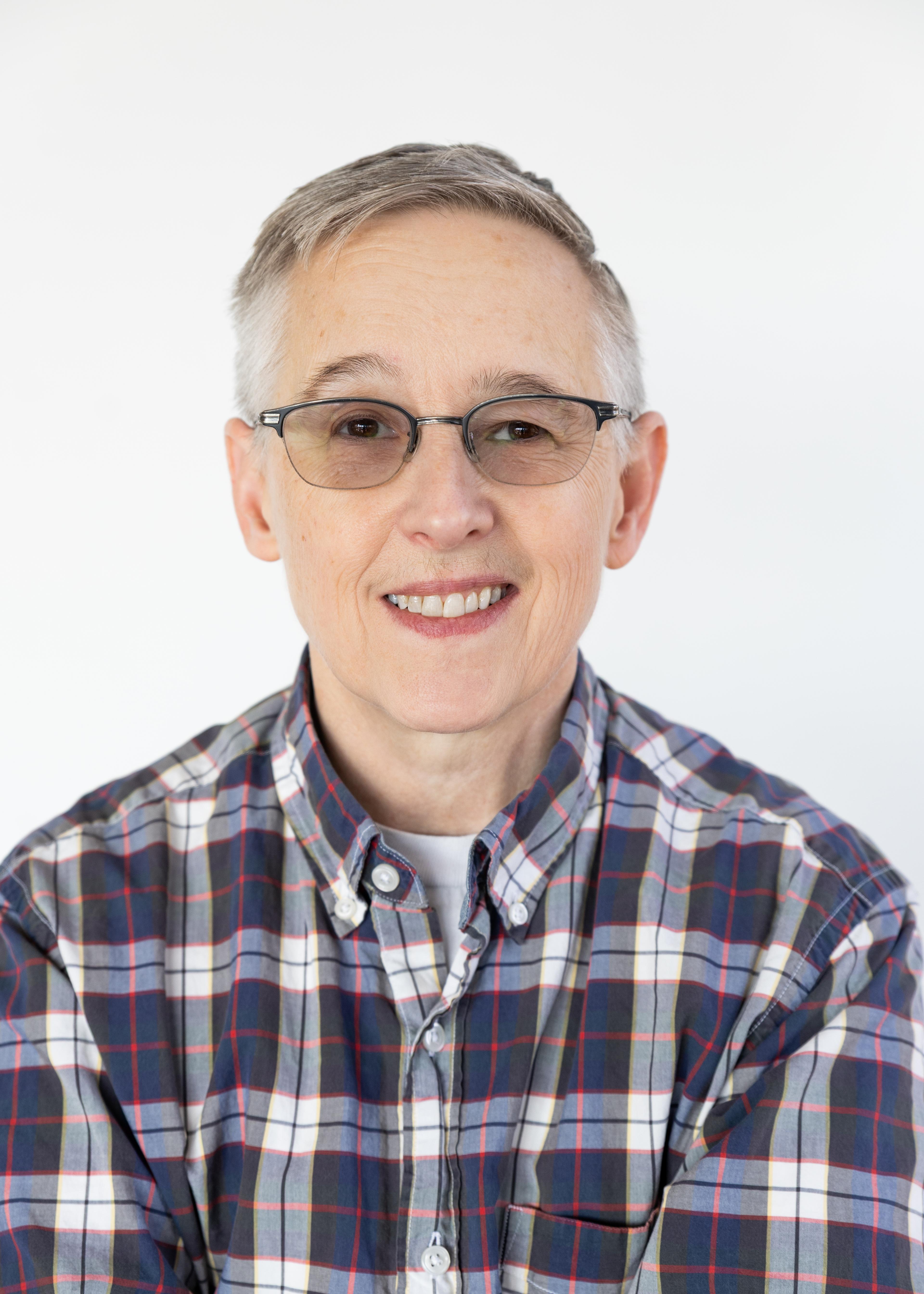 A color image of a person with short hair, glasses, and a plaid shirt smiling directly at the camera.