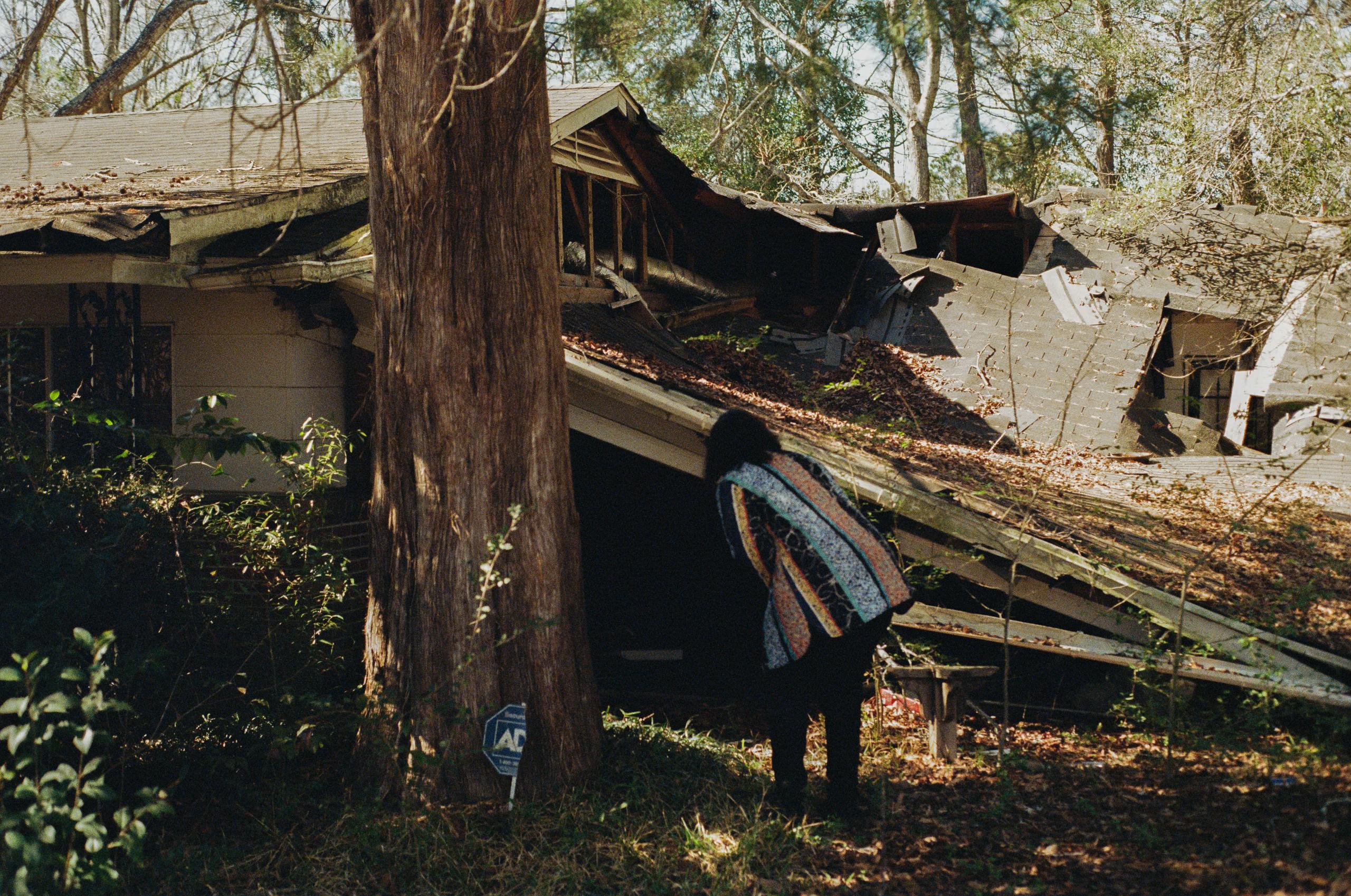 A woman leans over to investigate a decaying house.