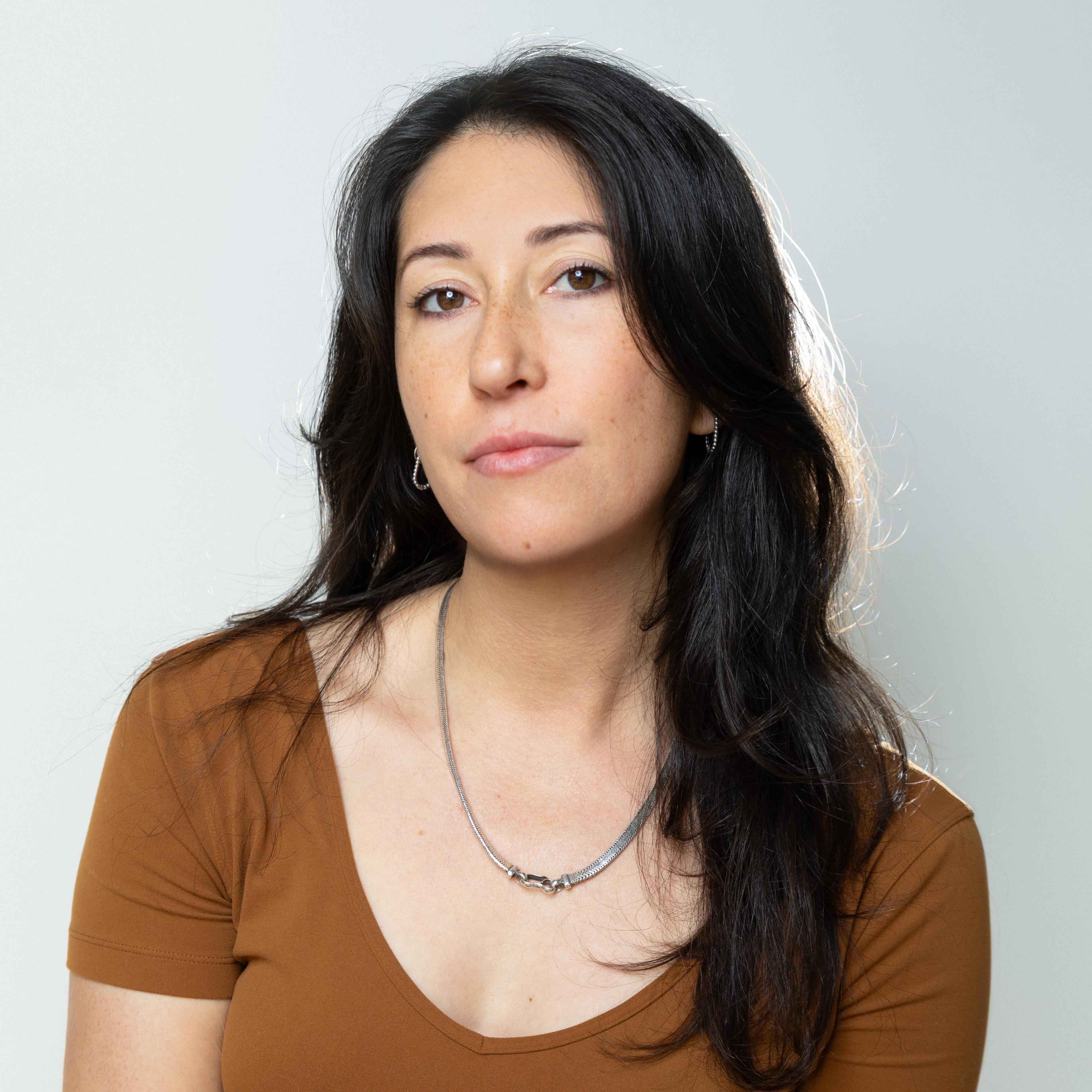A woman with dark hair looks into the camera.