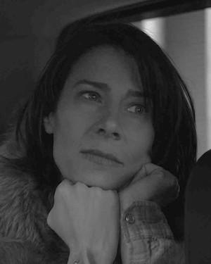 A black and white portrait of a woman resting her face in her hands. She looks off camera.